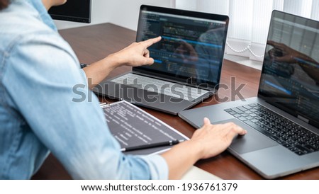 Asian programmer woman pointing and looking on multiple laptop screen to writing code and database while working about development website or applications in software development office