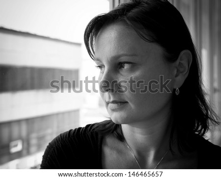 Sad woman looks out the window. Black and white portrait.