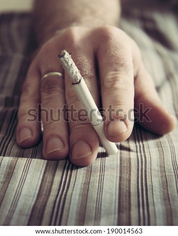 Cigarette in a man\'s hand.  Focus on the fingers. Warming filter