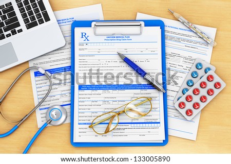 Doctor paperwork, medical healthcare and insurance concept: clipboard with prescription medicine drug claim form, office laptop, stethoscope, eyeglasses, blue pen and thermometer on wooden table