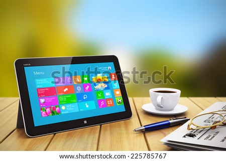 Mobile business internet communication and wireless office computer web work concept: modern tablet PC with touchscreen interface, newspaper, cup of coffee, pen and eyeglasses on wooden table outdoors