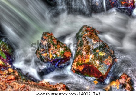 Neat looking rocks and leaves with smooth water running by in HDR High Dynamic Range