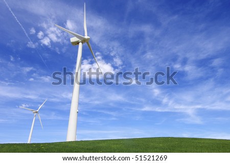 two windmills in a green meadow with blue sky