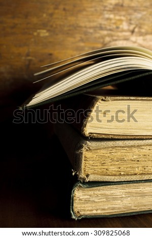 Stack of Old Books / An open book on top of a stack of three vintage books against a dark wood backdrop.
