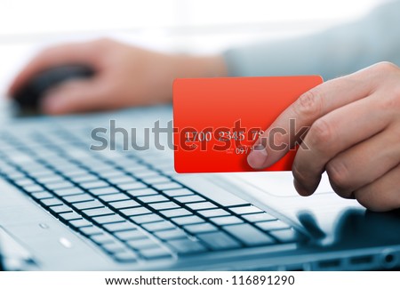 Man holding credit card in hand and entering security code using laptop keyboard