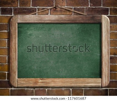Aged green blackboard hanging on brick wall as a background for your message