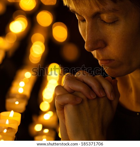 Prayer praying in Catholic church near candles. Religion concept.