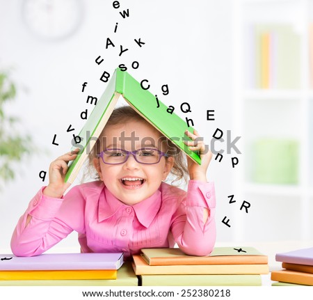 Smart smiling kid in glasses taking refuge under book roof from falling letters