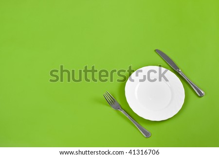 Knife, white round plate and fork on green background with free space