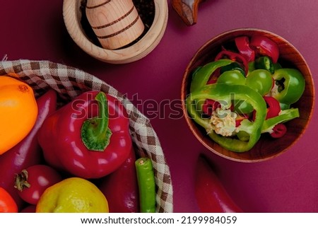 top view of pepper slices in bowl with vegetables as pepper tomato in basket with garlic crusher on bordo background Stok fotoğraf © 