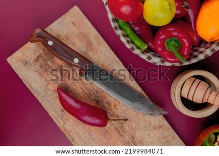 top view of pepper and knife on cutting board with vegetables in basket and garlic crusher on bordo background Stok fotoğraf © 