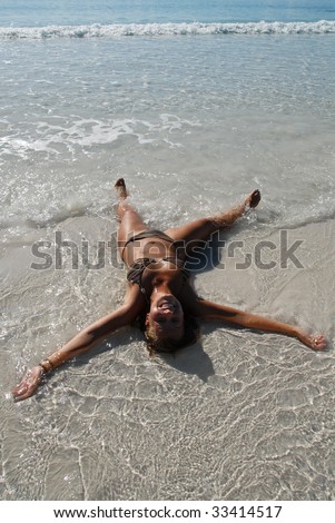 Cute teenage girl lying in water on a beach doing snow angel