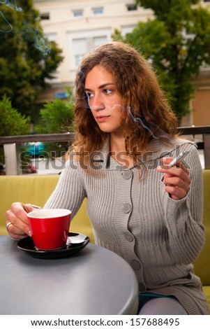 Young woman drinking coffee and smoking cigarette outdoors