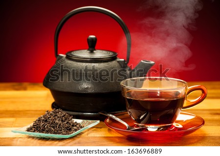 a cup of black tea with teapot in the background