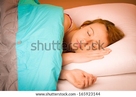 Woman lying on pillow in bed, covered with blue blanket
