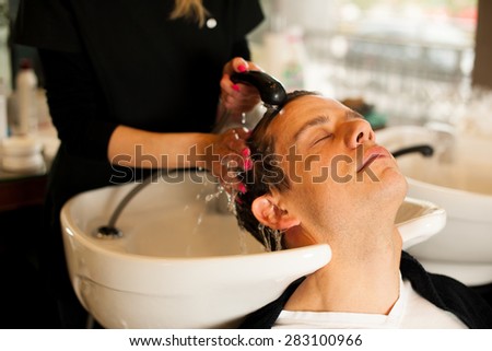 Female hairdresser washing hair of smiling man client at beauty salon