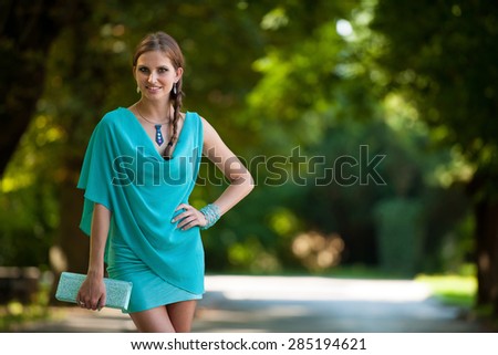 Blog style beautiful brunette woman in fashionable dress posing in park presenting garment