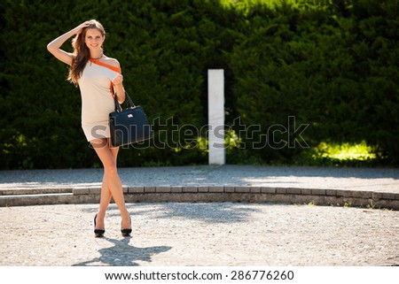 Blog style beautiful brunette woman in fashionable dress posing in park presenting garment