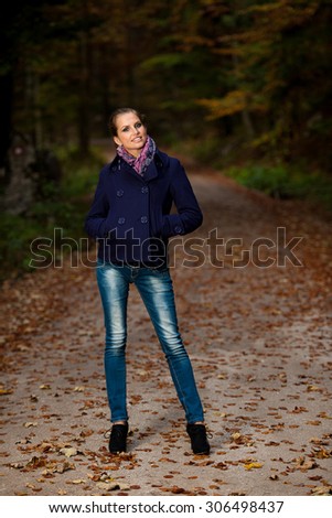 Pretty young woman on a walk in forest on late autumn day in fashionable dress