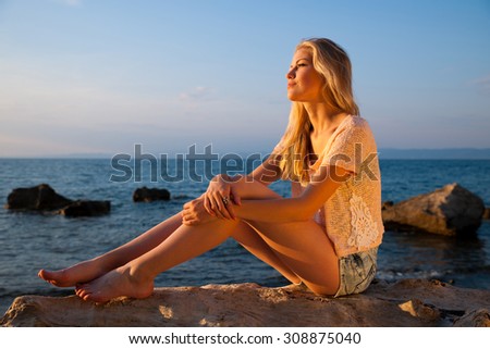 Beautiful young blonde woman resting on a beach at dusk in summer - sea side sunset