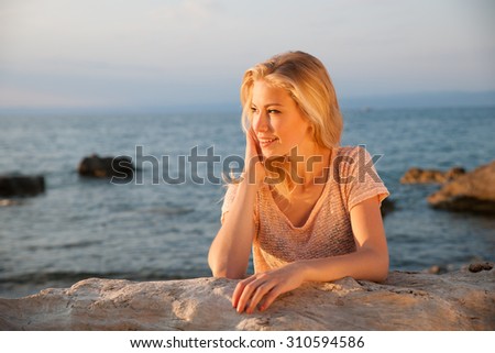 Beautiful young blonde woman resting on a beach at dusk in summer - sea side sunset