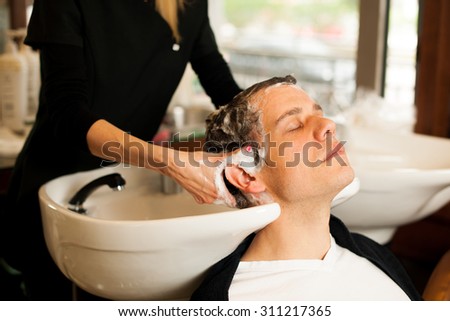 Female hairdresser washing hair of smiling man client at beauty parlour
