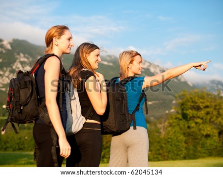 Backpackers on travel - Group of three cute young girls with backpacks on a trip across grass field