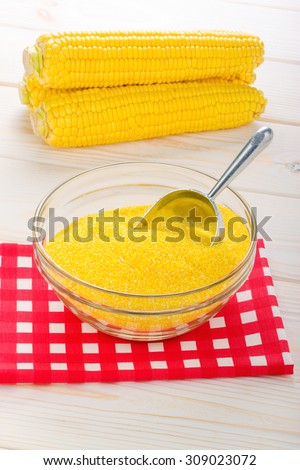 corn grits in a transparent plate with ears of corn on the wooden background