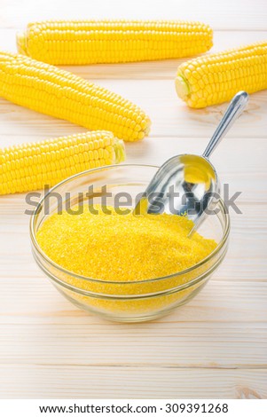 corn grits in a transparent plate with ears of corn on the wooden background