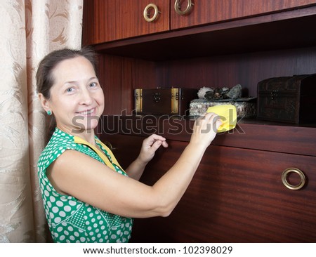 Mature woman cleans a furniture indoor