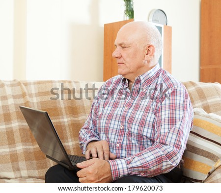elderly gray-haired man  at his laptop on  sofa at home