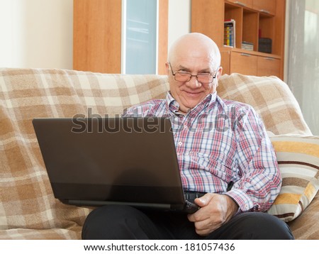 elderly gray-haired man working at his laptop on  sofa at home