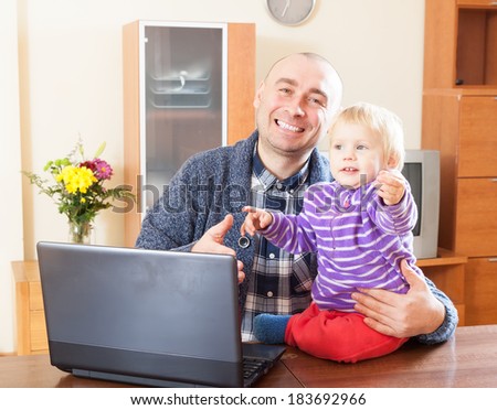dad sitting at  laptop with  young daughter on his lap