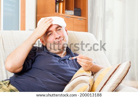 Illness  man with thermometer stupes  towel to  head at home