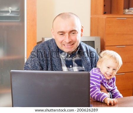Adult dad sitting at  laptop with  young daughter on his lap