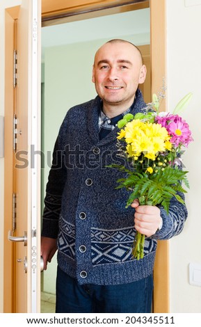 Adult smiling man with  bouquet of flowers near  door