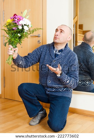 guilty  man kneeling with  bouquet of flowers.