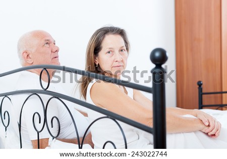 Sad mature woman  turned away from   elderly man sitting on   bed