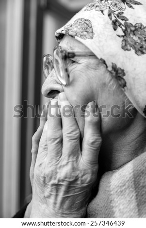 elderly woman in   scarf and  glasses near window at home.