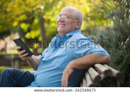 Portrait of senior  man   reading on   bench during autumn day.