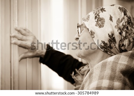 elderly woman in   scarf and  glasses near window at home.