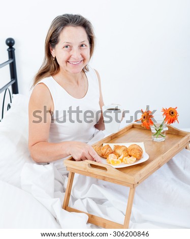 Beautiful older woman having breakfast in   bedroom on   bed.