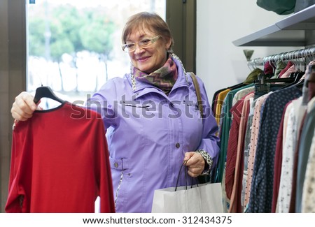 Mature woman choosing     blouse in   clothing store.