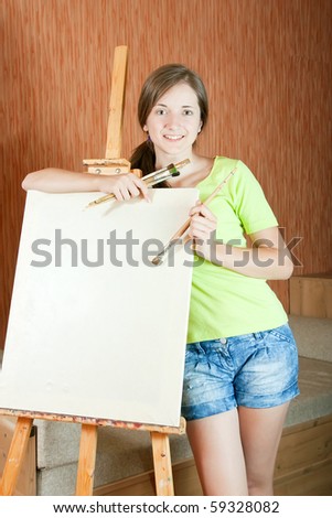 Pretty girl with brushes standing  near easel indoor