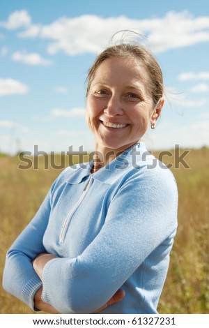 Mature woman in blue smiling against summer landscape