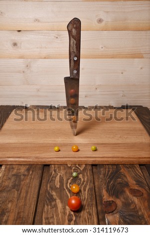Abstract food art composition of different size tomatoes and knife on wooden background.