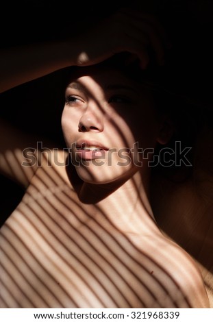 Close up portait of beautiful girl wearing bra. Sunlight through jalousie shines on beautiful woman\'s face.