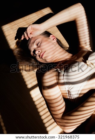 Portrait  of young blonde in bra liying on the floor. Sunlight through jalousie shines on beautiful woman\'s face.