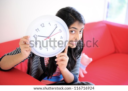 pretty Indian girl showing time in her clock sitting with piggy bank