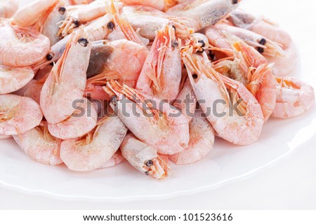 Pile of frozen shrimps on plate, closeup on white